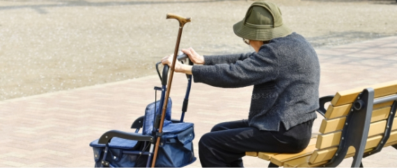 ベンチに座り休憩する、杖を持った高齢者