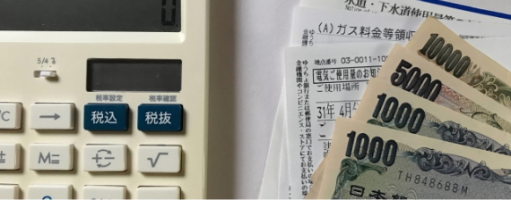 電卓と光熱費料金表と現金の写真
